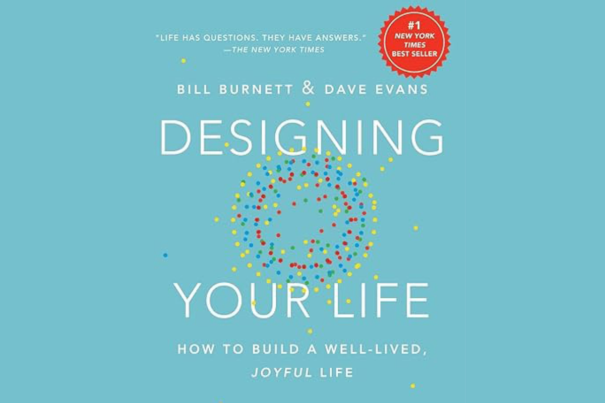 Hardcover book titled "Designing Your Life: How to Build a Well-Lived, Joyful Life" by Bill Burnett & Dave Evans. The blue cover features the words “DESIGNING YOUR LIFE” in large white letters, overlaid with concentric circles of yellow dots on the outside, blue dots for next ring, and red dots for the innermost ring.